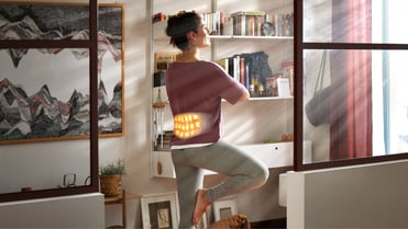 Eine Frau in einer stehenden Yoga-Position trägt unter ihrem T-Shirt einen ThermaCare Wärmegürtel