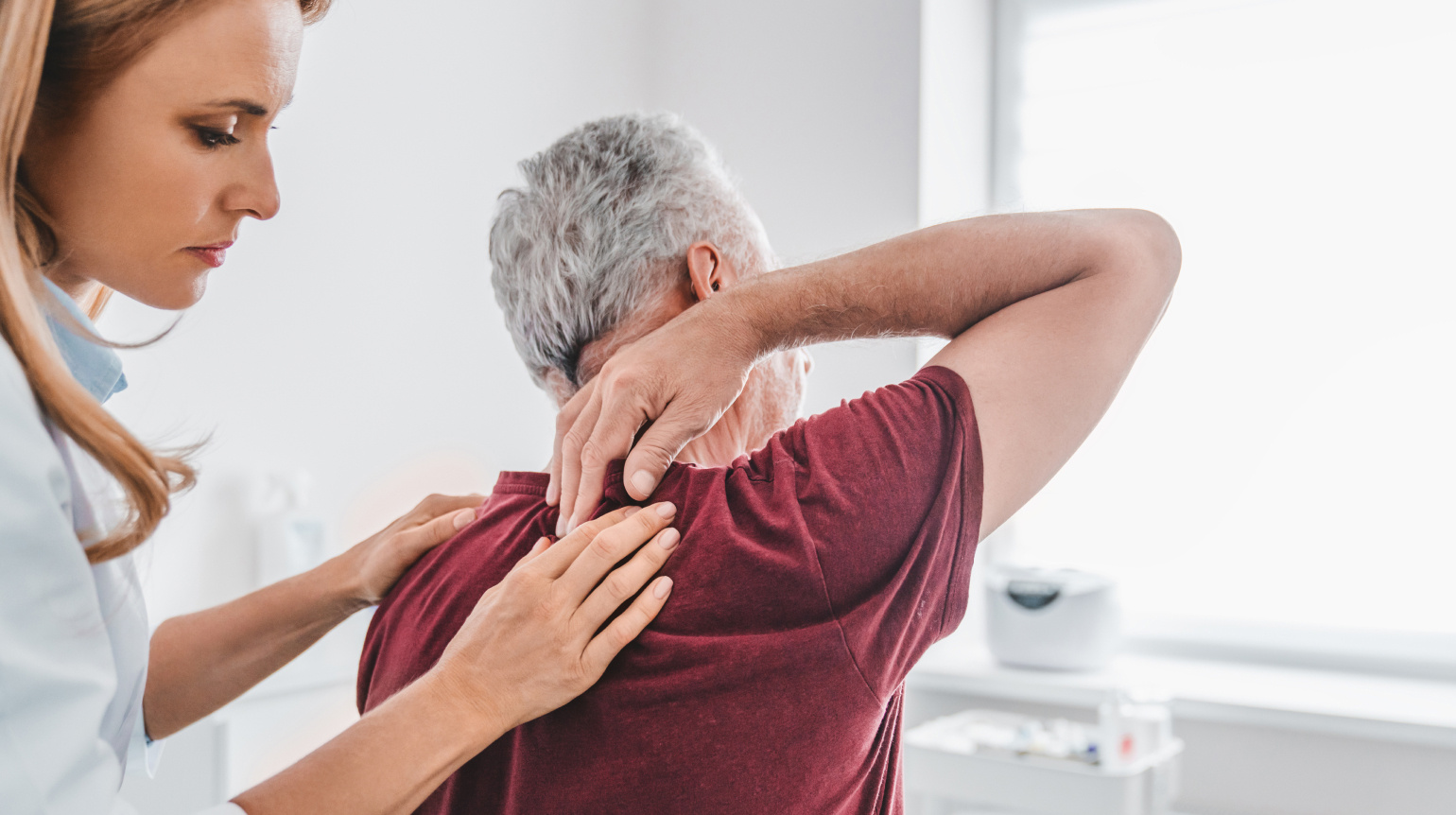 Seitenansicht auf Therapeutin, die die Hände auf die Schultern des vor ihr sitzenden Patienten legt. Dieser legt von oben rechte Hand auf rechte Schulter.