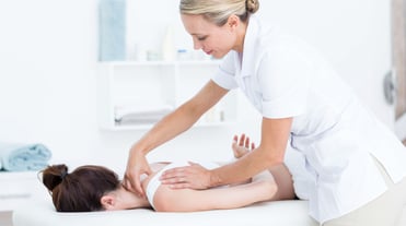 Therapeutin beugt sich über die Patientin, die vor ihr auf dem Bauch liegt und bearbeitet ihre Nacken-Schulterregion mit den Händen.