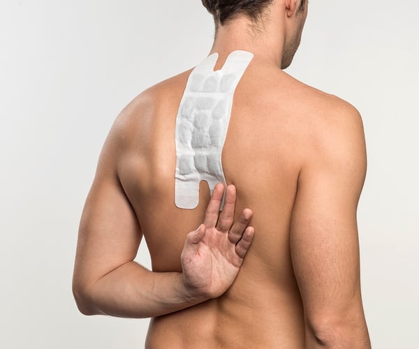 Mann mit freien Oberkörper fixiert ThermaCare® Wärmeauflage für größere Schmerzflächen mit dem Handrücken von unten auf der Haut