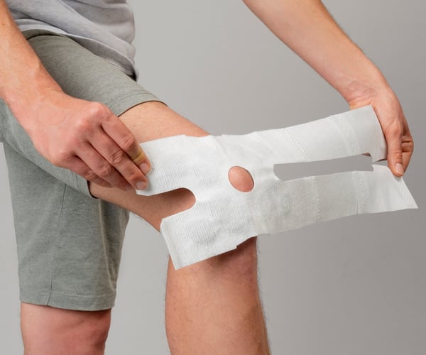 Eine Person platziert den ThermaCare Wärmeumschlag auf dem Knie 