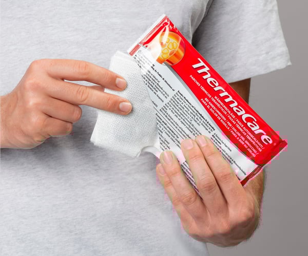 Eine Person nimmt einen ThermaCare Wärmeumschlag aus der Packung 