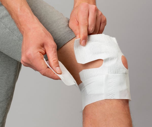 Eine Person befestigt den Klettverschluss des ThermaCare Wärmeumschlags auf der Vorderseite des Knies