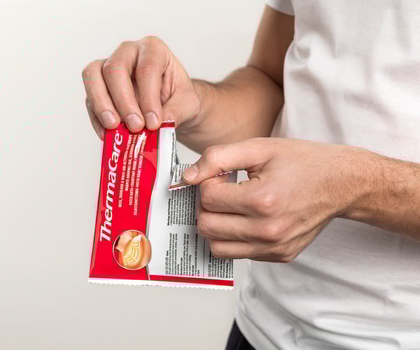 Person öffnet Verpackung einer ThermaCare® Wärmeauflage für Nacken und Schulter