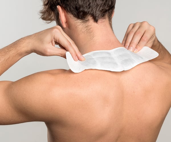 Mann mit freiem Oberkörper klebt sich ThermaCare® Wärmeauflage auf den Nacken