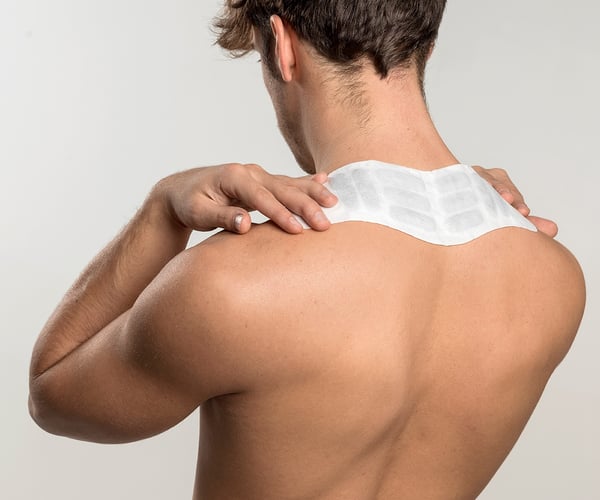 Mann mit freiem Oberkörper fixiert ThermaCare® Wärmepflaster am Nacken 