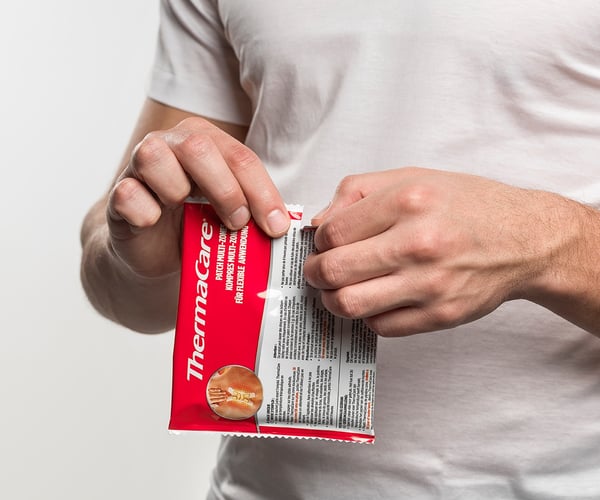 Person öffnet Verpackung einer ThermaCare® Wärmeauflage für flexible Anwendung