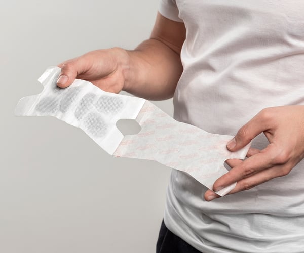 Person entfernt Schutzfolie einer ThermaCare® Wärmeauflage für flexible Anwendung