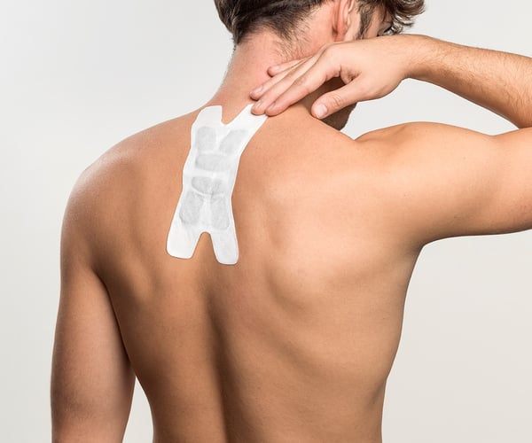 Mann mit freien Oberkörper klebt sich ThermaCare® Wärmeauflage für flexible Anwendung auf den oberen Rücken