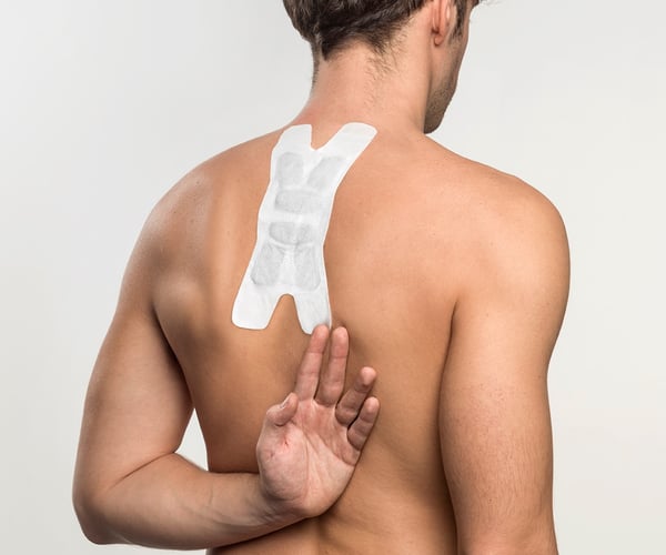 Mann mit freien Oberkörper fixiert ThermaCare® Wärmeauflage für flexible Anwendung mit dem Handrücken