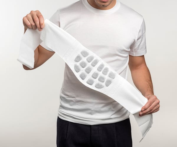 Mann in weißem T-Shirt klappt ThermaCare® Wärmeumschlag bei Rückenschmerzen komplett aus