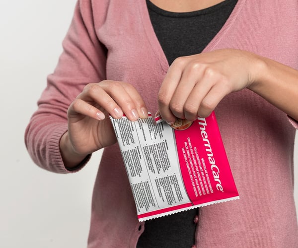 Frau öffnet Verpackung einer ThermaCare® Wärmeauflage bei Regelschmerzen