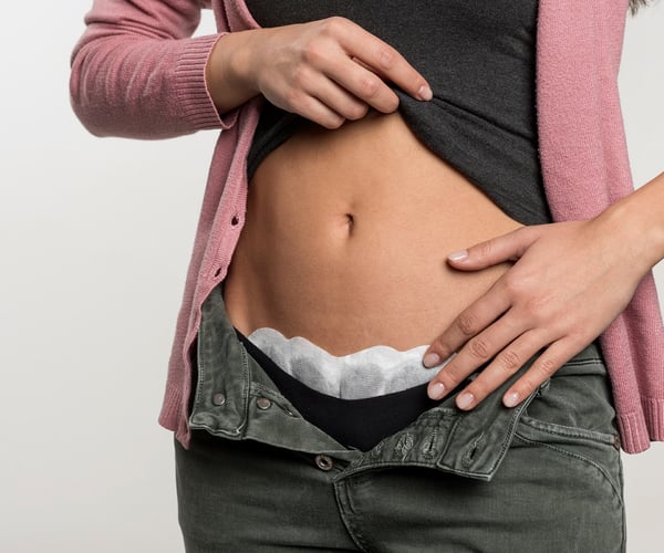 Frau klebt ThermaCare® Wärmeauflage bei Regelschmerzen von innen an ihren Slip