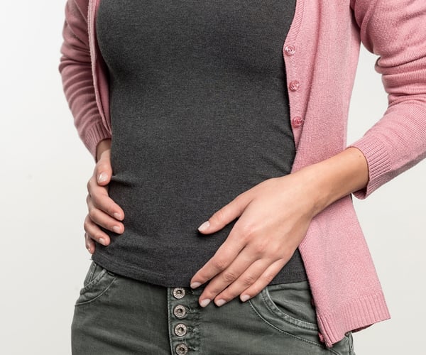 Frau mit grünem Oberteil und weißer Hose; ThermaCare® Wäremeauflage bei Regelschmerzen ist nicht zu sehen