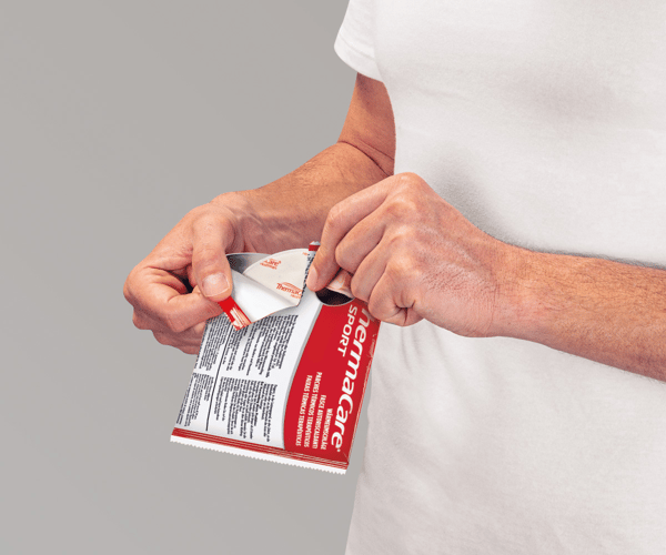 Eine Person reißt die Verpackung eines ThermaCare Wärmepflasters für Sport auf