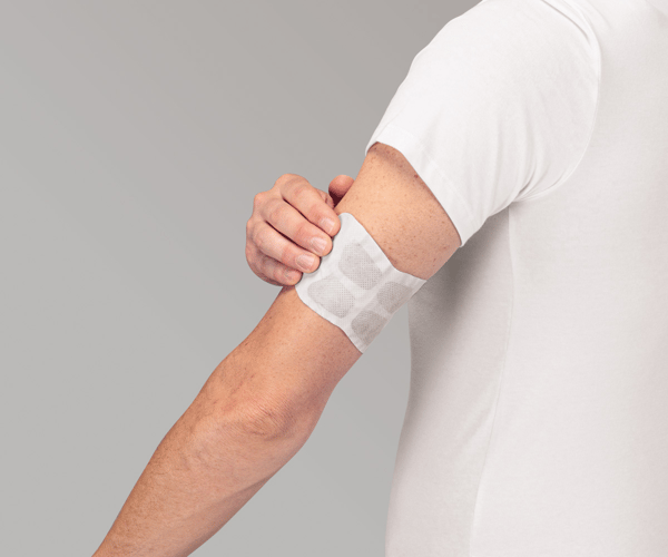 Eine Person klebt ThermaCare Sport auf den Oberarm
