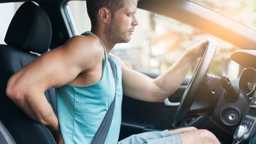 Ein Mann sitzt am Steuer eines Autos und hält seine rechte Hand auf seinen Rücken