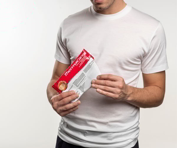 Person in weißem T-Shirt öffnet Verpackung der ThermaCare® Wärmeumschläge für den Rücken
