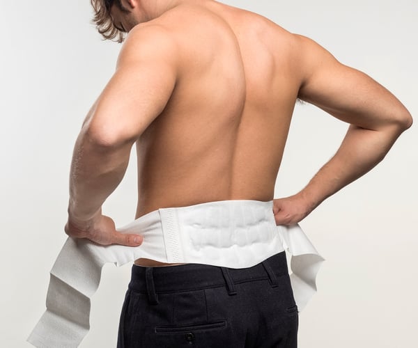 Mann mit freiem Oberkörper legt ThermaCare® Wärmeumschlag gegen Rückenschmerzen von hinten um