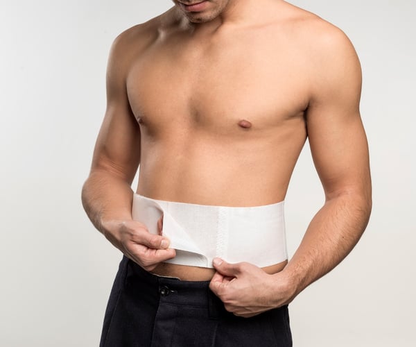 Mann mit freiem Oberkörper schließt den Kletterverschluss des ThermaCare® Wärmeumschlags gegen Rückschmerzen an der Vorderseite des Körpers