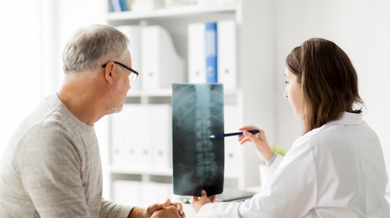 Eine Ärztin zeigt einem Patienten ein Röntgenbild seiner Brustwirbelsäule