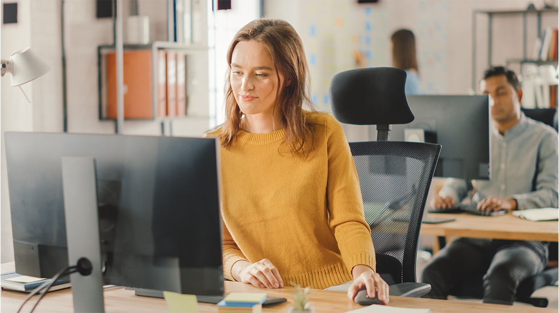 richtig-sitzen-am-schreibtisch-eine-frau-traegt-einen-orangefarbenen-pullover-und-arbeitet-am-computer