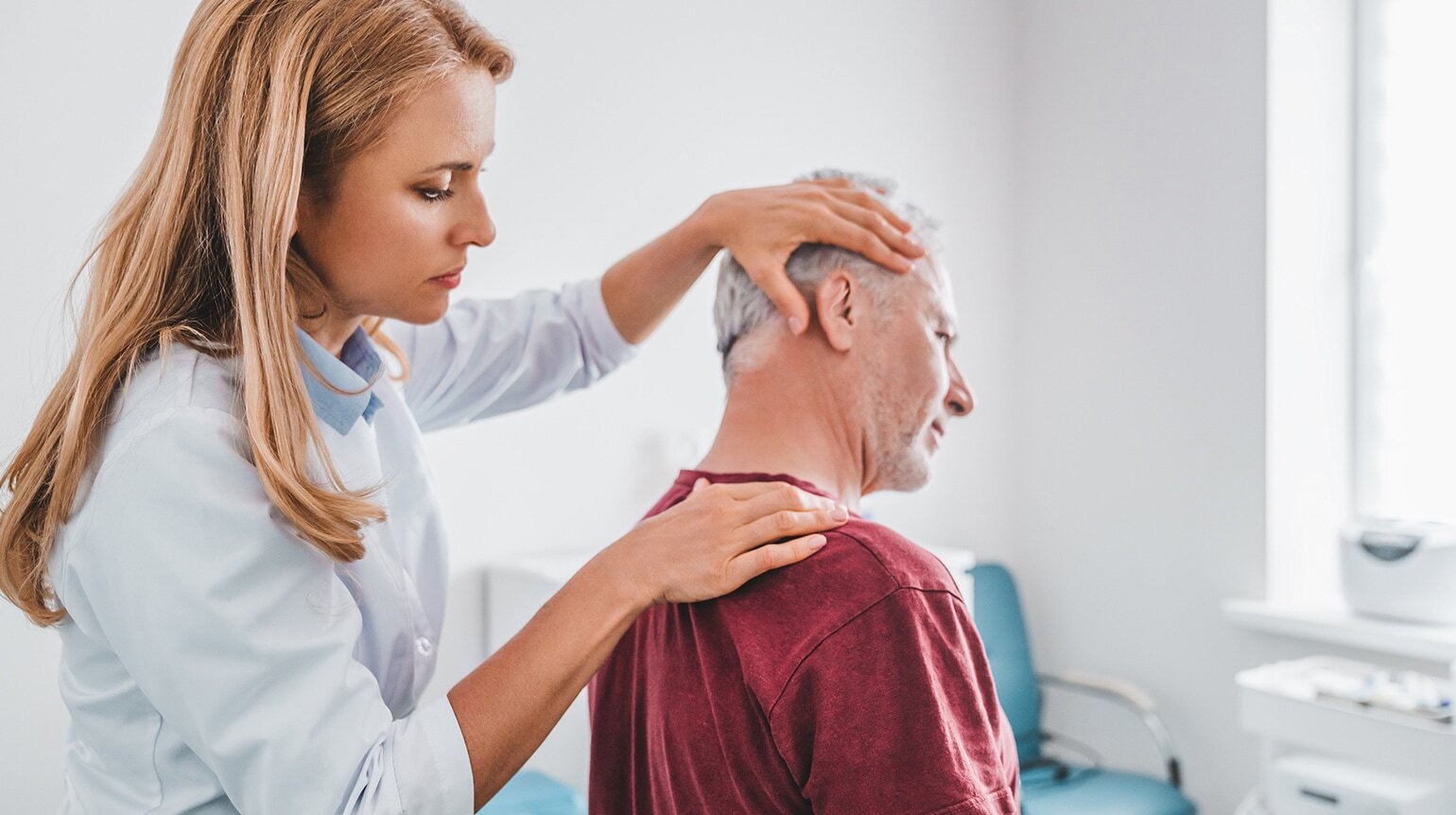 Ärztin untersucht mit beiden Händen Nacken und Schultern eines Patienten und prüft damit die Beweglichkeit der Halswirbelsäule Ärztin untersucht mit beiden Händen Nacken und Schultern eines Patienten und prüft damit die Beweglichkeit der Halswirbelsäule