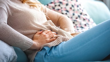 Eine Frau greift sich mit den Händen an ihren schmerzenden Unterleib.