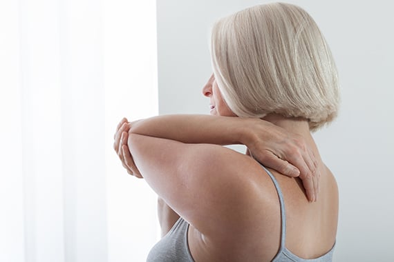 Eine Frau mit Kurzhaarschnitt fasst sich mit der linken Hand an ihre Schulter