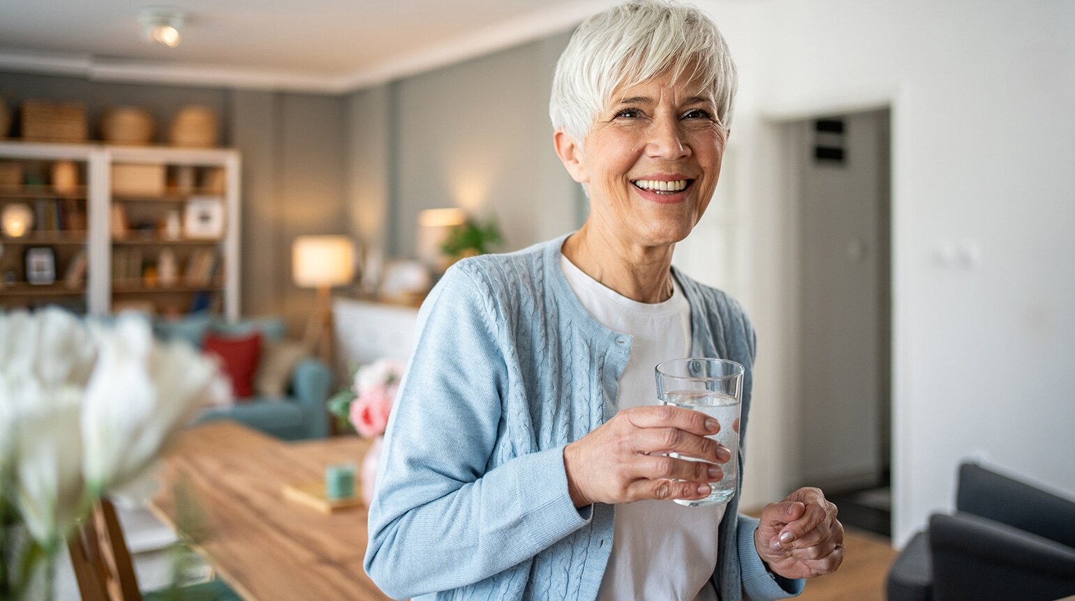 Ältere Frau mit kurzen grauen Haaren lächelt und hält ein Glas Wasser mit einer sich auflösenden Magnesiumbrausetablette in der Hand Ältere Frau mit kurzen grauen Haaren lächelt und hält ein Glas Wasser mit einer sich auflösenden Magnesiumbrausetablette in der Hand