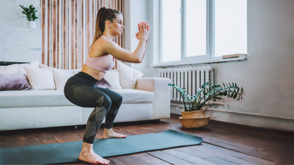 Eine Frau macht Kniebeugen auf einer Gymnastikmatte in einem Wohnzimmer