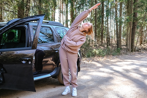 Eine Frau macht Dehnuebungen neben einem Auto 