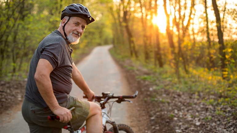 Ein Mann blickt bei Sonnenschein von seinem Fahrrad aus in die Kamera