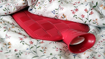 Eine rote Wärmflasche liegt auf einer geblühmten Bettdecke