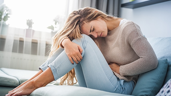 Frau sitzt auf der Couch und hat Schmerzen