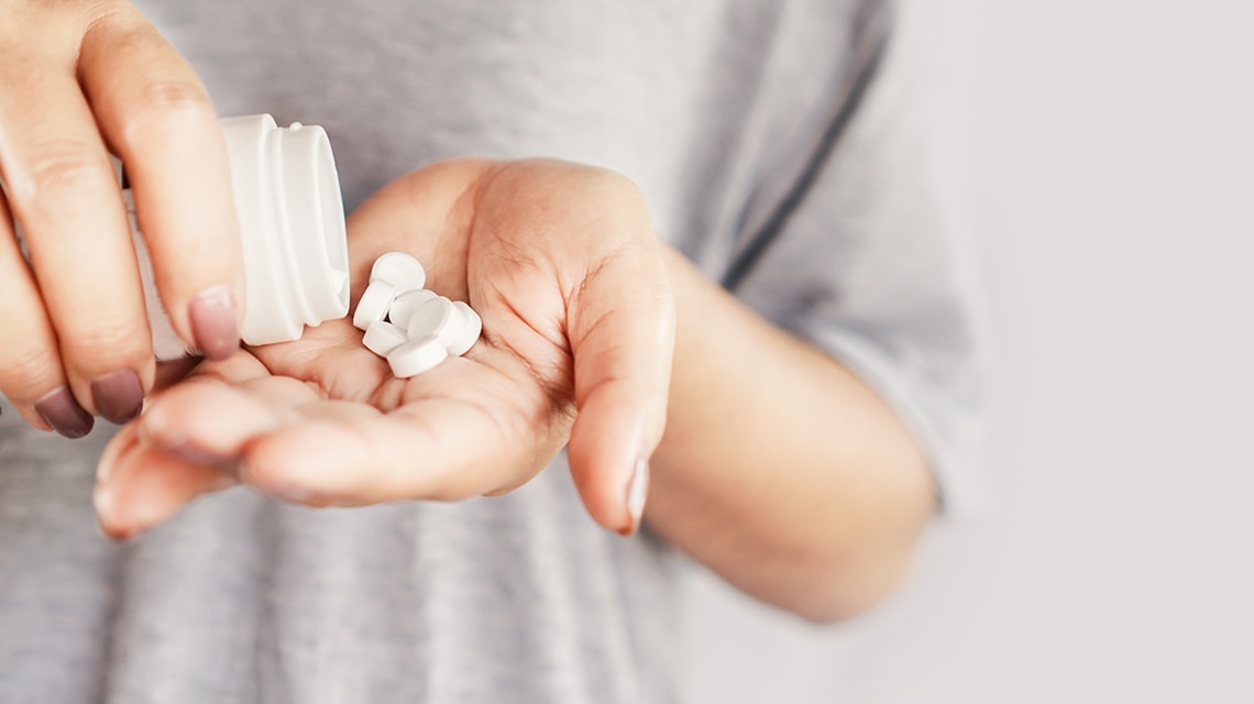 Eine Frau hält schüttet Schmerztabletten aus einer Dose in ihre Handfläche