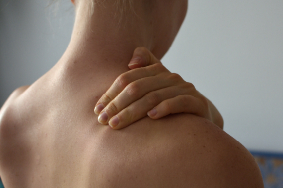 Nahaufnahme des Rueckens einer Frau, die sich mit der linken Hand den rechten Schulter Nacken Bereich haelt Nahaufnahme des Rueckens einer Frau, die sich mit der linken Hand den rechten Schulter Nacken Bereich haelt