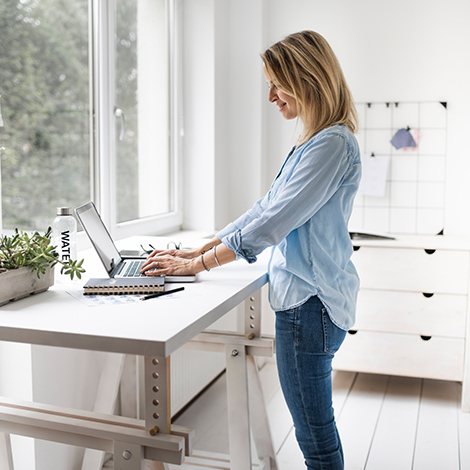 Eine blonde Frau arbeitet im Stehen an ihrem Schreibtisch