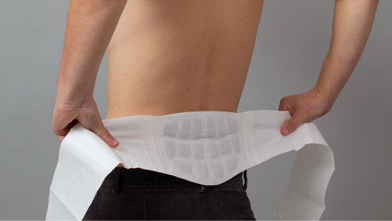 Person mit freiem Oberkörper legt sich ThermaCare® Wärmeumschlag am unteren Rücken an Person mit freiem Oberkörper legt sich ThermaCare® Wärmeumschlag am unteren Rücken an